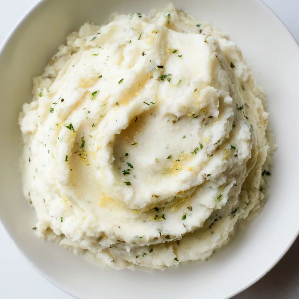 Creamy cauliflower mash with garlic and lemon, garnished with fresh herbs, ready to serve.