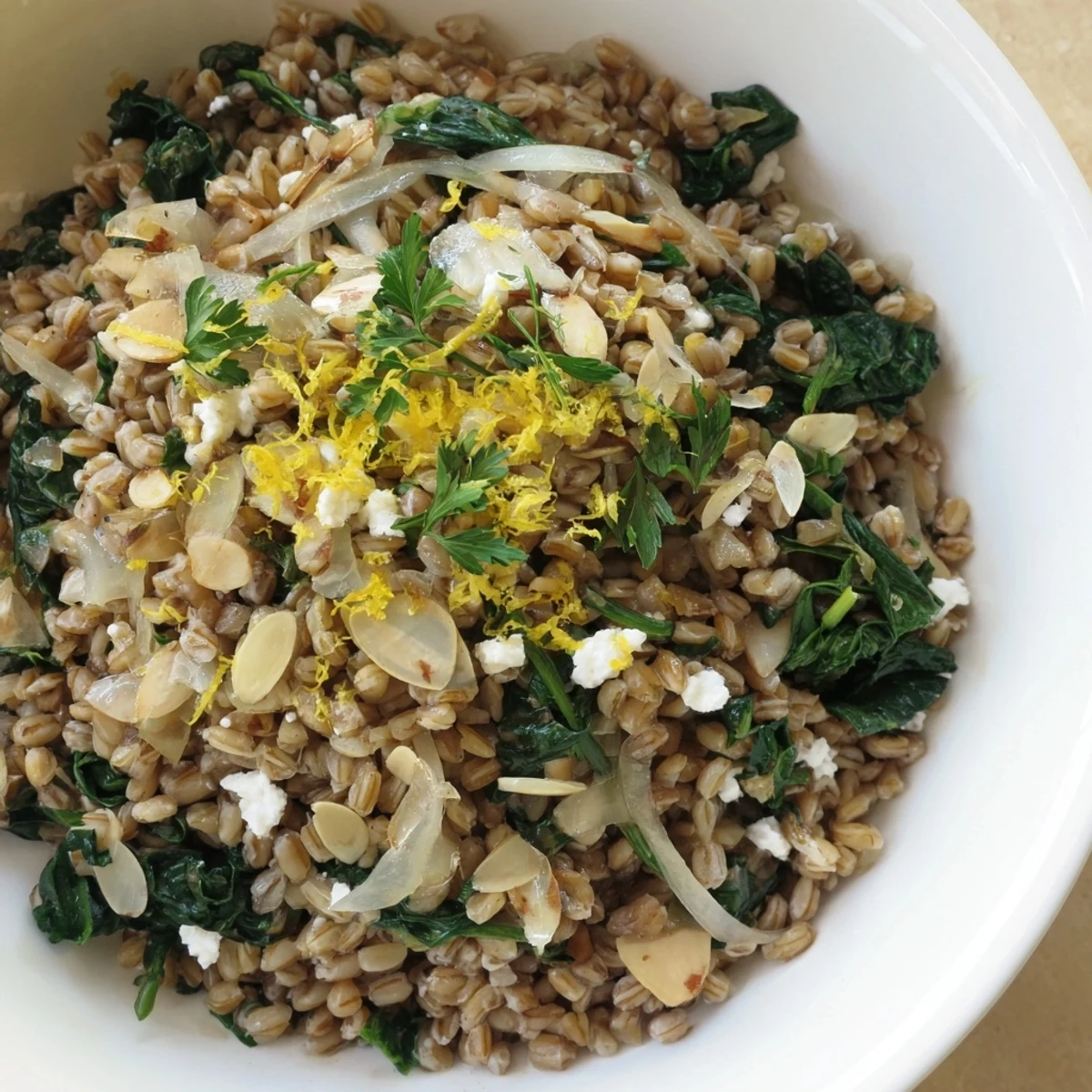 A steaming bowl of warm Farro & Greens Pilaf topped with toasted, fragrant almonds.