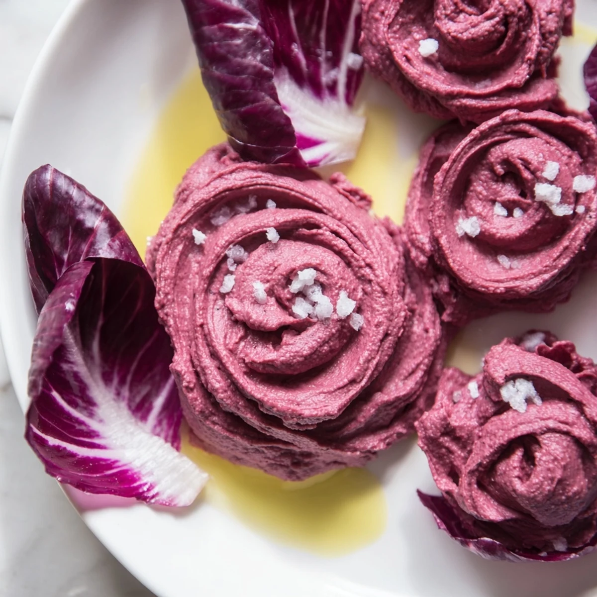 A savory plate of The Velvet Rose: smooth beet hummus garnished with olive oil and served cool.