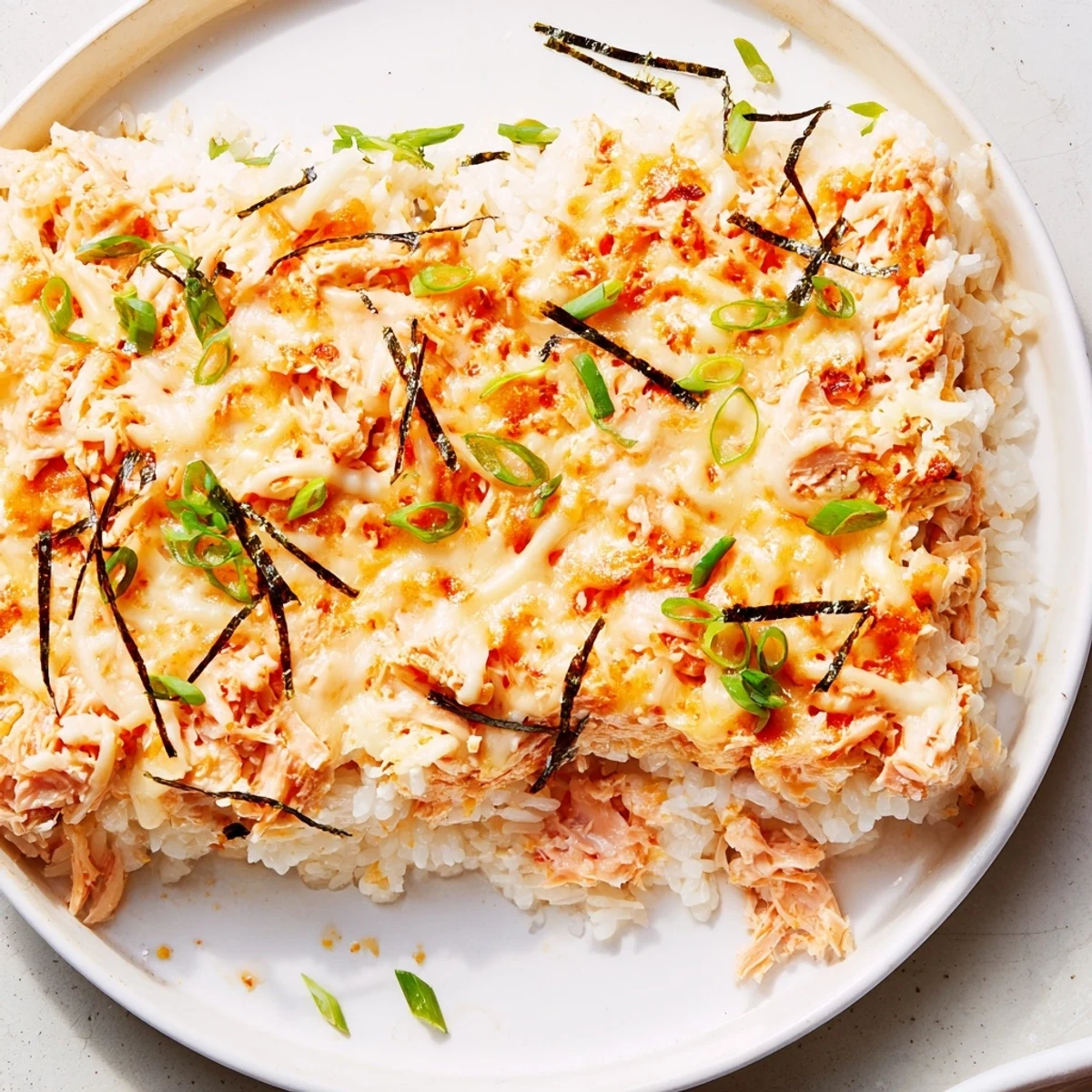 A close-up of a creamy layered Creamy Salmon Sushi Bake, featuring golden cheese and flaky fish.