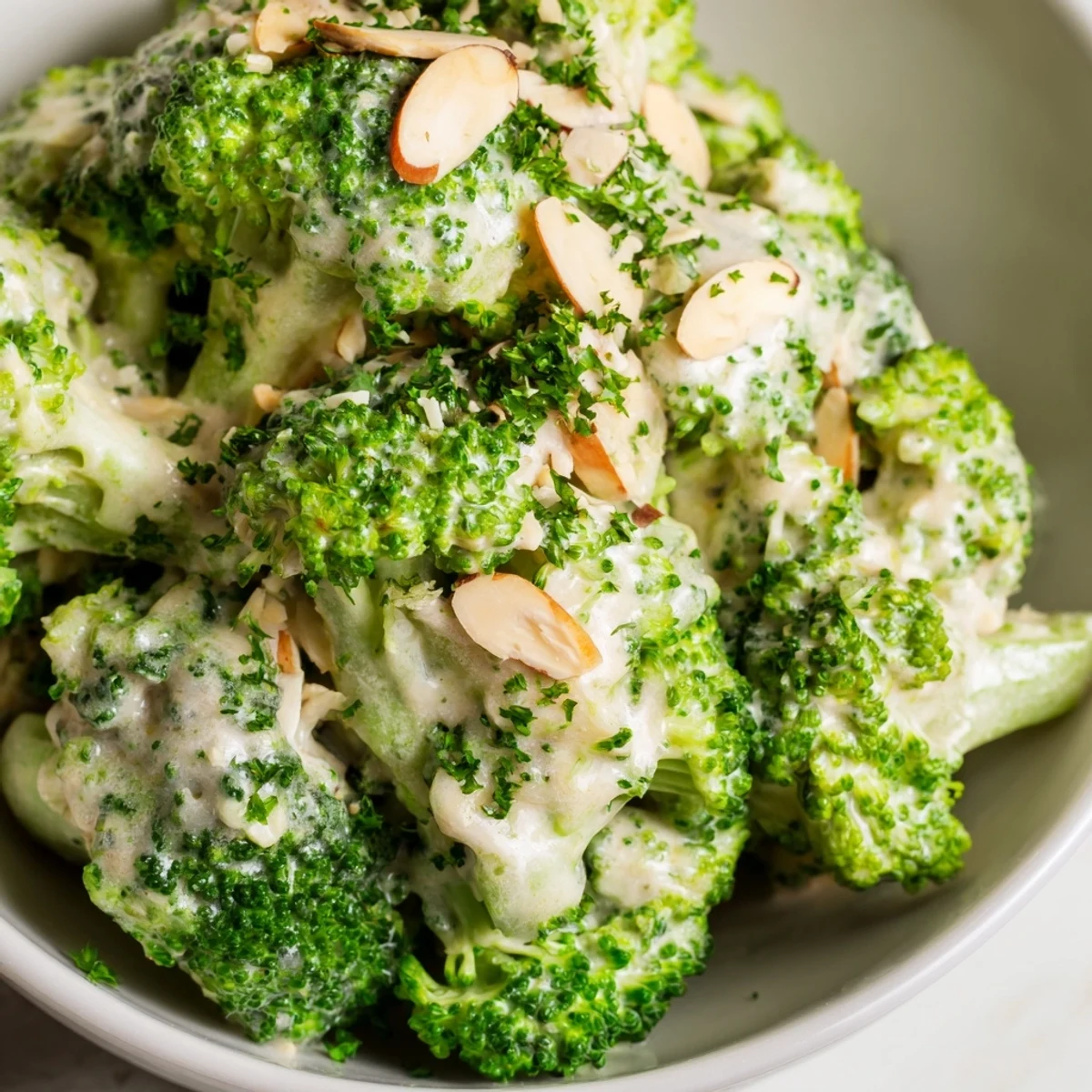 Creamy Garlic Parmesan Broccoli Salad with crisp-tender blanched florets, red onion, and tomatoes tossed in a rich dressing, topped with toasted almonds and fresh parsley garnish.
