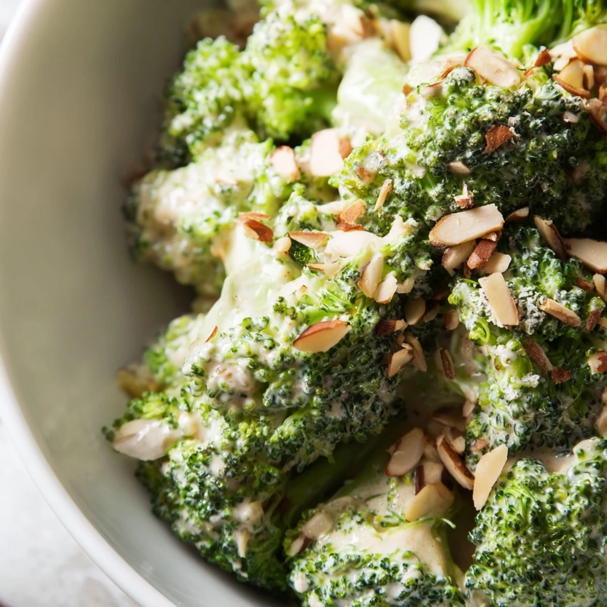 A bowl of chilled Garlic Parmesan Broccoli Salad featuring bright green broccoli, creamy yogurt dressing with minced garlic, Parmesan cheese, slivered almonds, and a sprinkle of fresh parsley.