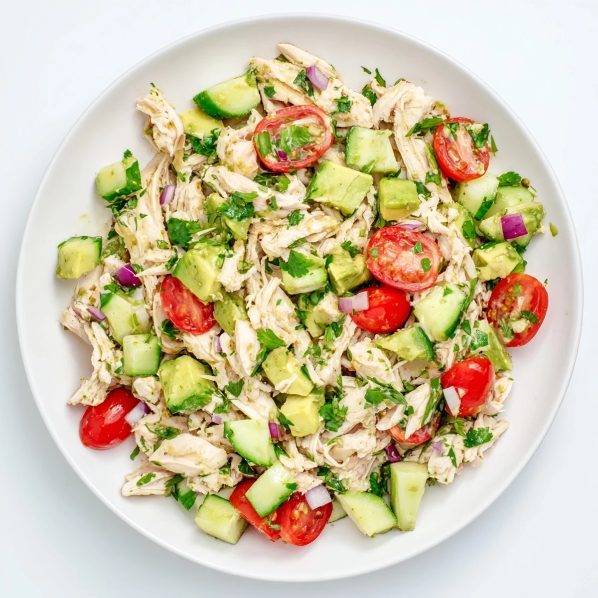 Creamy avocado chicken salad in a white bowl, topped with fresh cilantro and juicy cherry tomatoes.