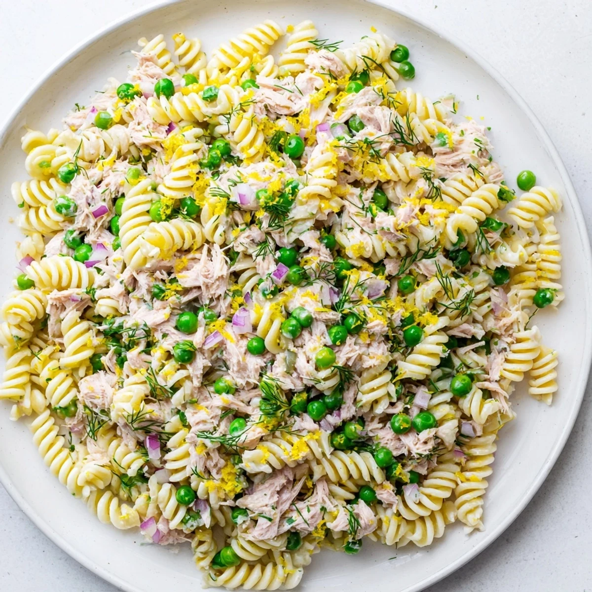 A vibrant bowl of Lemony Tuna Pasta Salad with tender fusilli, flaked tuna, bright green peas, and fresh herbs tossed in a zesty lemon vinaigrette.  