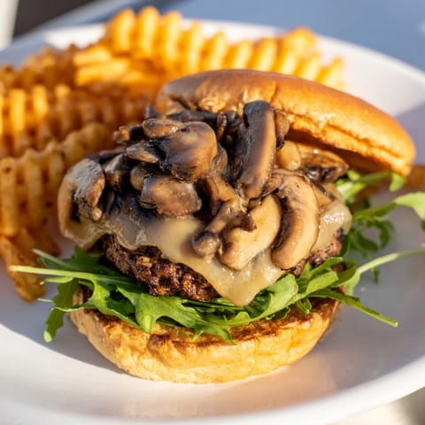 Golden-brown waffle fries accompany a juicy Mushroom Swiss Burger with a flavorful, cheesy topping.