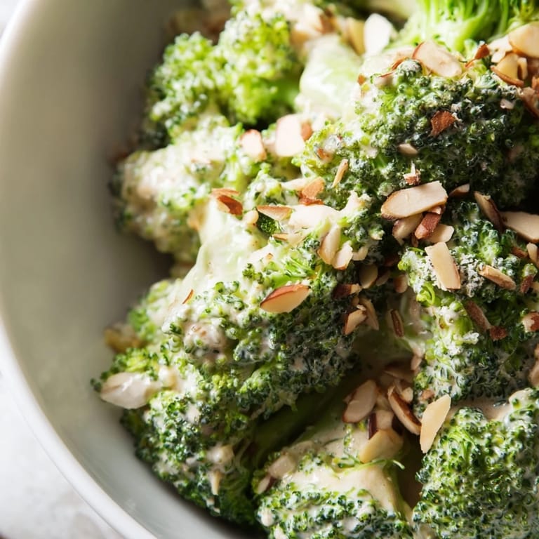 A bowl of chilled Garlic Parmesan Broccoli Salad featuring bright green broccoli, creamy yogurt dressing with minced garlic, Parmesan cheese, slivered almonds, and a sprinkle of fresh parsley.